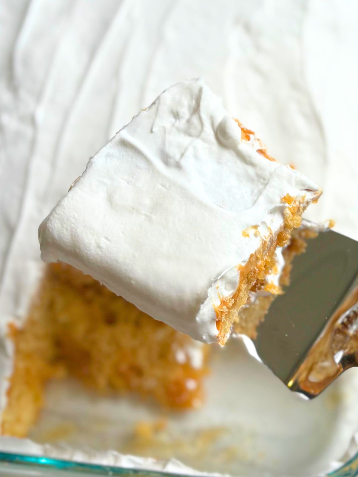 a slice of salted caramel poke cake being lifted out of the pan