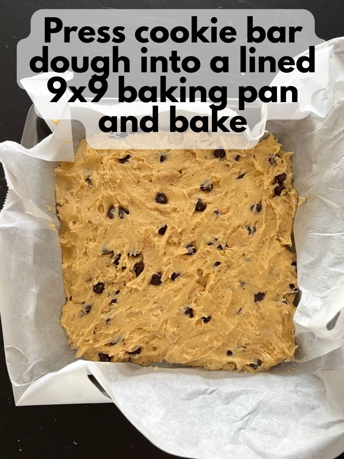cookie bar dough pressed into a square pan lined with parchment paper