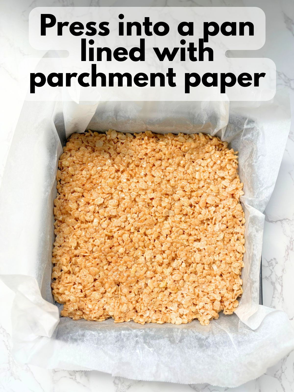 peanut butter rice krispie treats pressed into a square pan lined with parchment paper