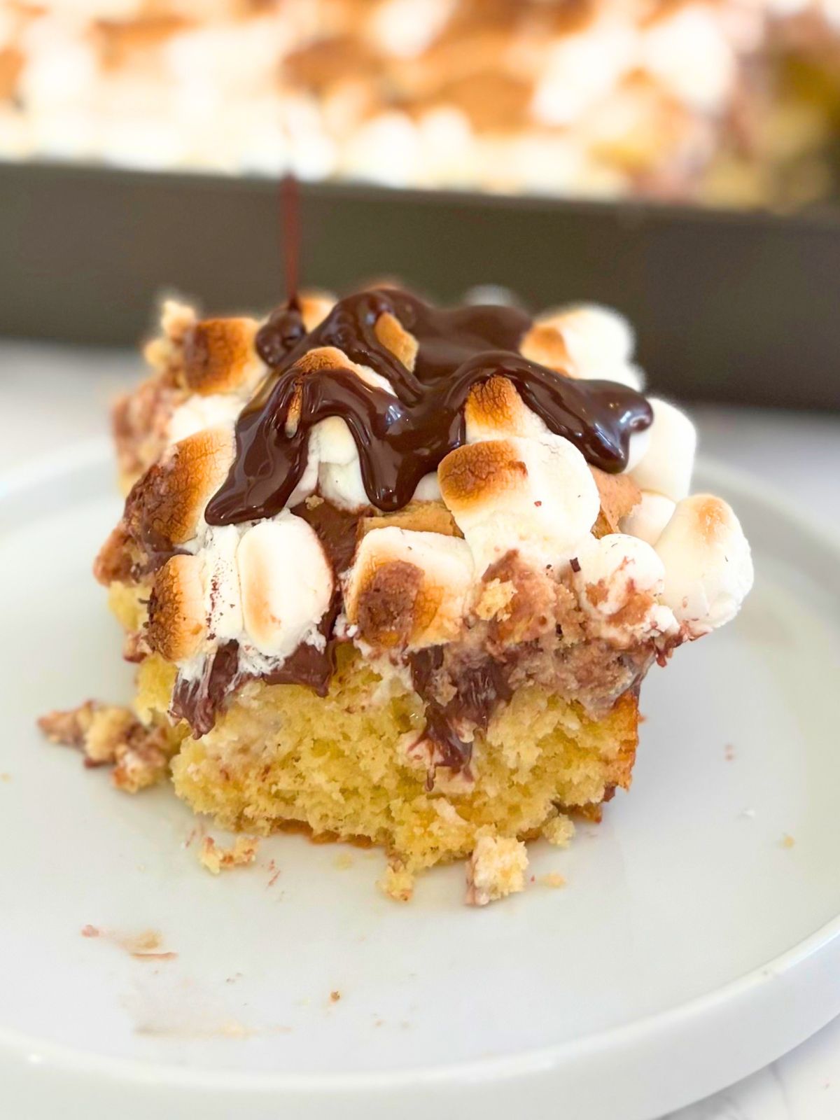 a slice of s'mores poke cake drizzled with hot fudge