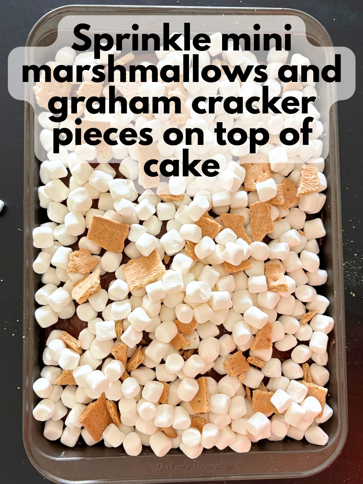 marshmallows and graham cracker pieces spread over the top of a baked and frosted cake