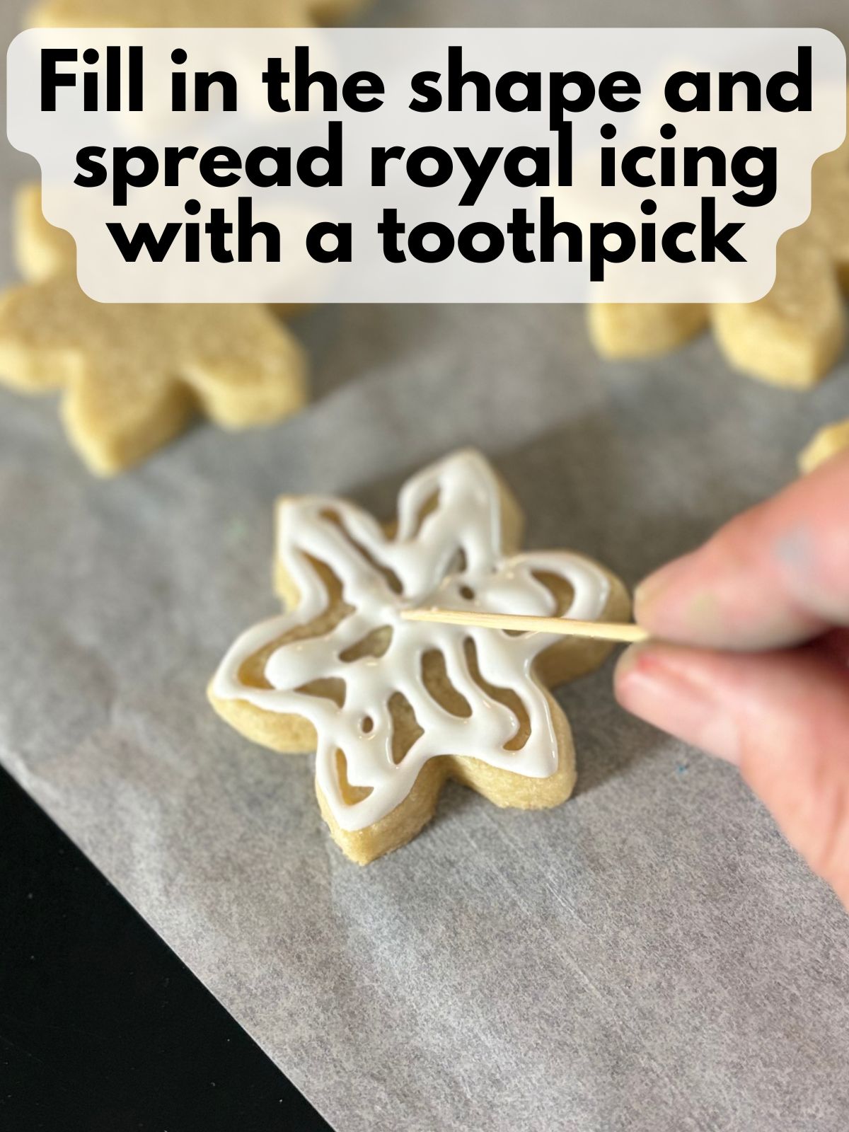 more royal icing filling in the middle of the snowflake shape with a toothpick spreading the royal icing